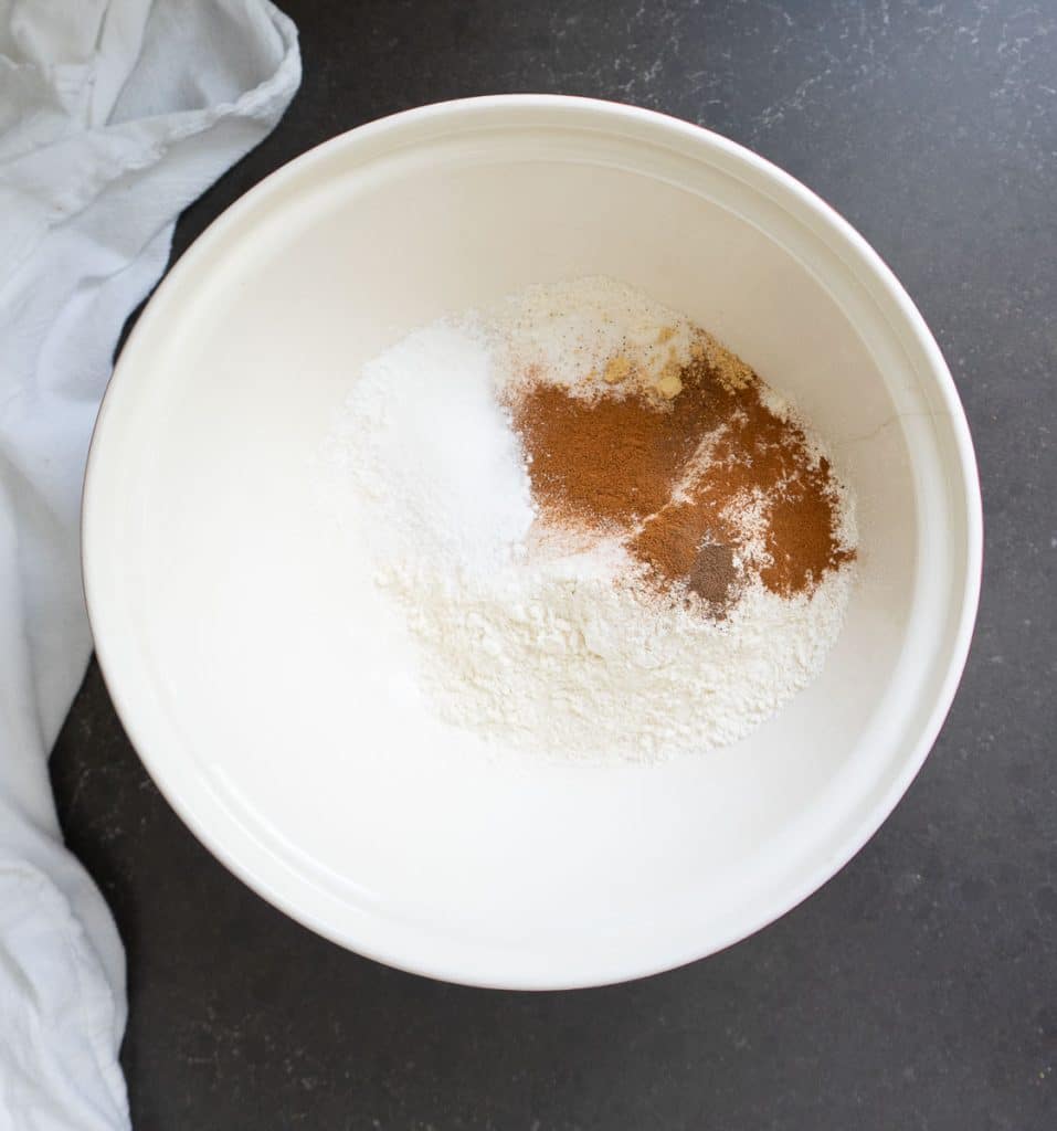flour, and spices for loaded pumpkin scones in a white bowl on a black countertop there is a white tea towel in the left side of the photo