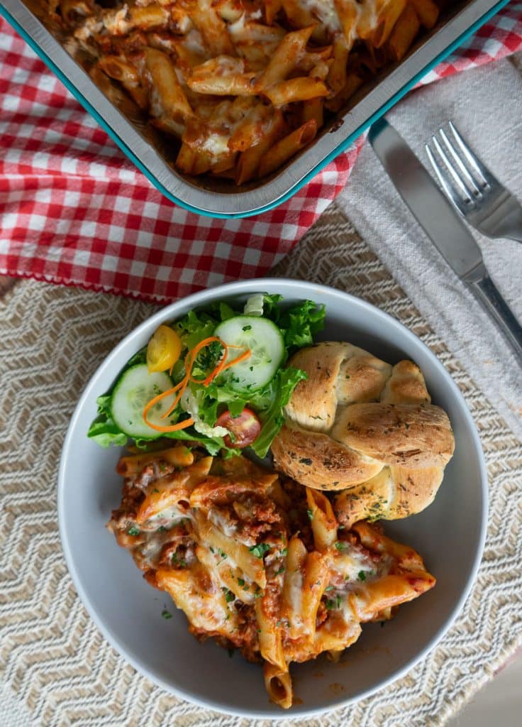 op view of plated mostaccioli and a green salad on the side with a garlic roll a corner of the casserole dish is visible in the upper right corner