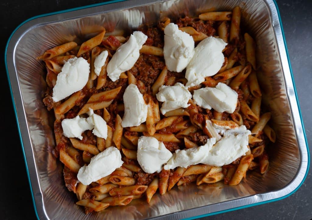 dollops of ricotta cheese across the top of mostaccioli noodles and sauce in a 9x13 baking pan