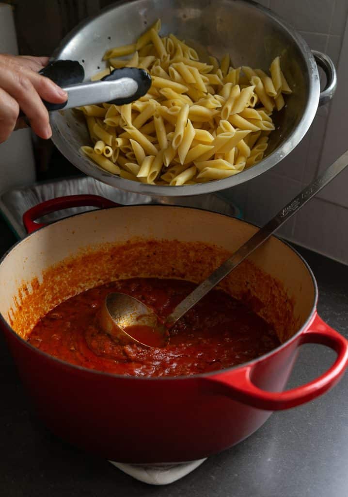 putting mostaccioli noodles into meat sauce