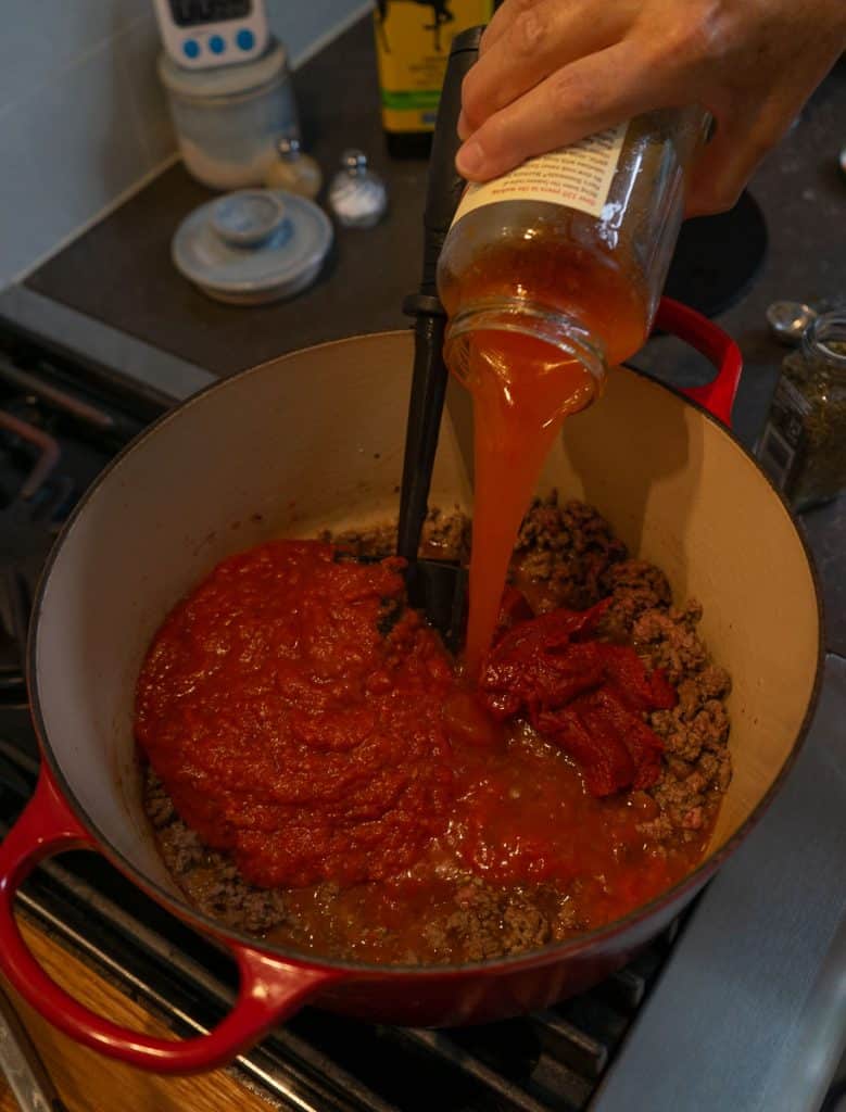 pouring marinara into dutch oven with browned ground beef and tomato paste