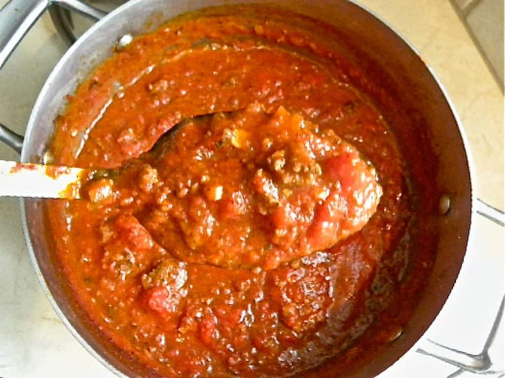 spoon with spaghetti sauce on it over a pot of spaghetti sauce