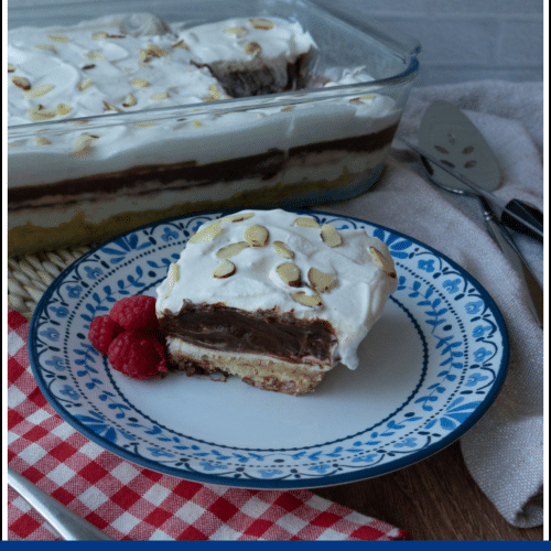 serving of dessert on a plate with a red checked napkin the left with a fork and the dish of dessert with one square cut out in the background