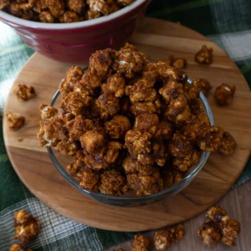 bowl of caramel corn on a wood cutting board with caramel corn on strewn around the bowl