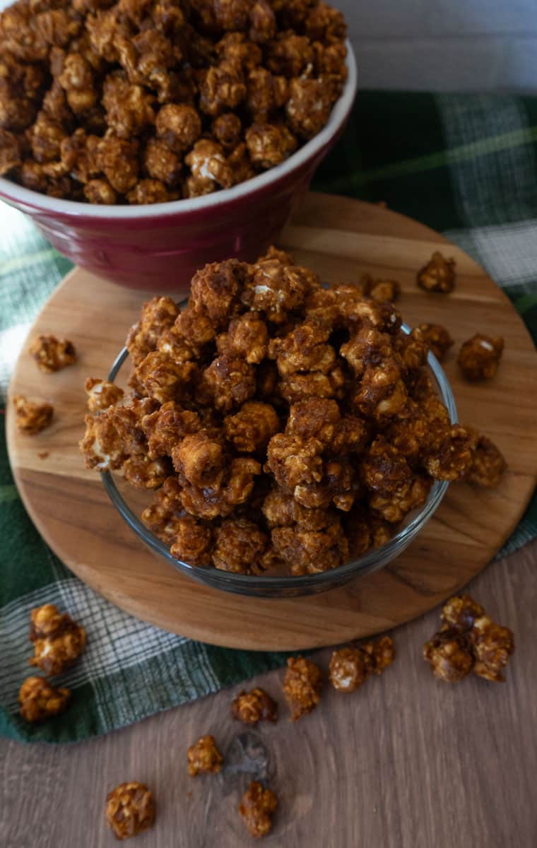 bowl of caramel corn on a wood cutting board with caramel corn on strewn around the bowl