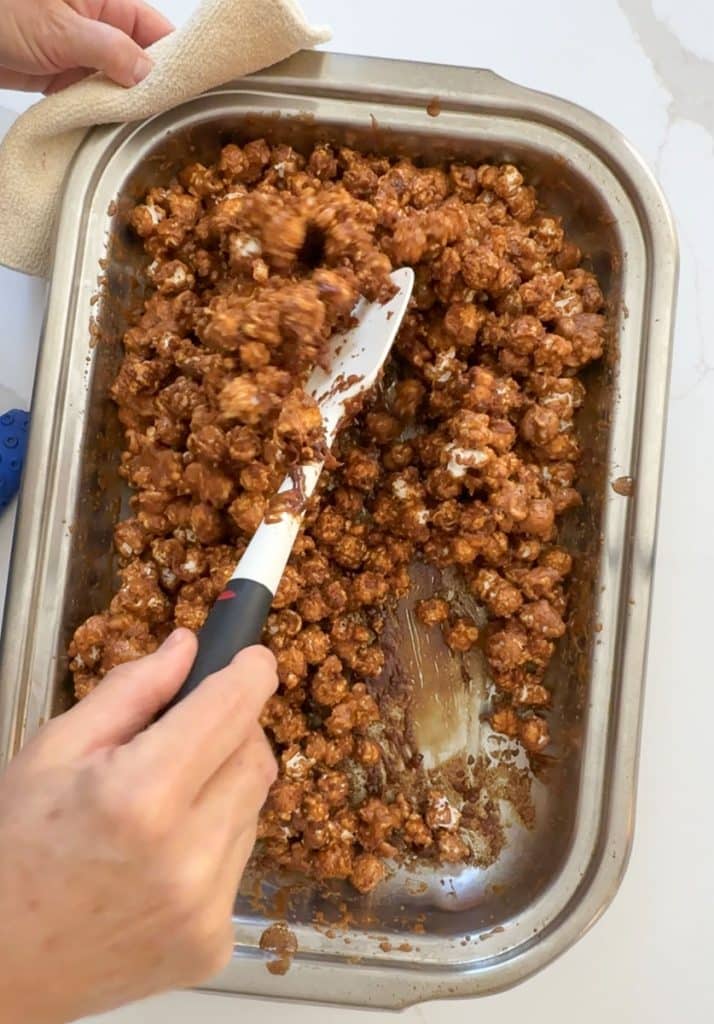 folding caramel over popcorn in a roasting pan