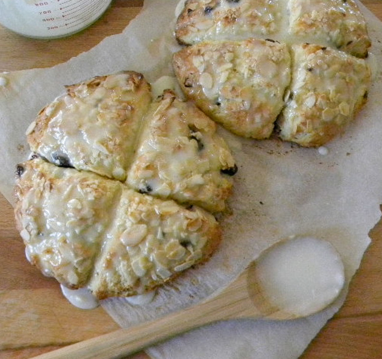 cherry scones on parchment paper with a wooden spoon in the lower section of the photo with icing on it