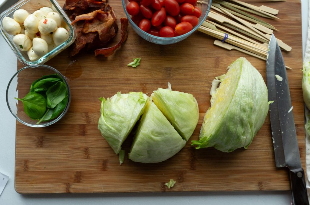 dividing head of iceberg lettuce into 6 small wedges with large knife on wood cutting board