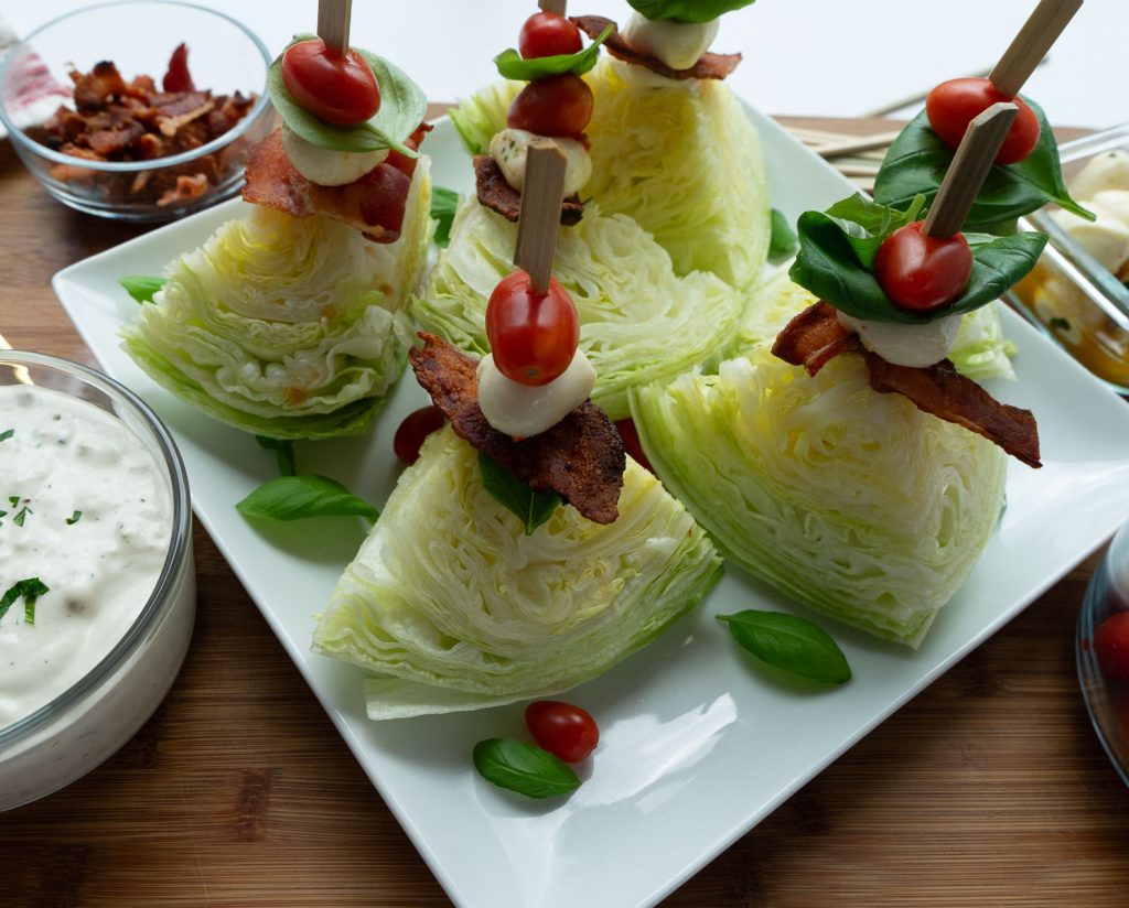 mini wedge salad skewers on a white platter with dressing in bowl on the side