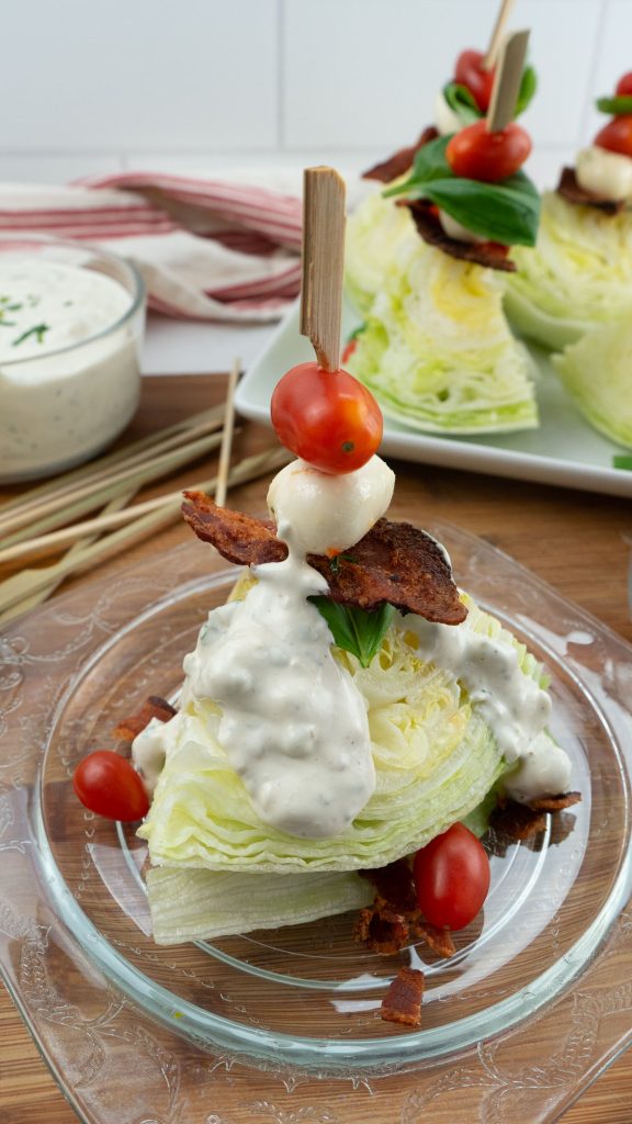 mini wedge salad on a glass place with platter of salad in back ground