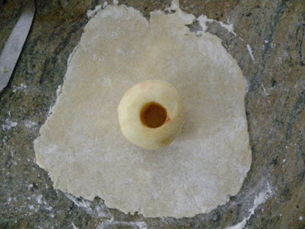 peeled and cored apple setting in the center of rolled out pastry