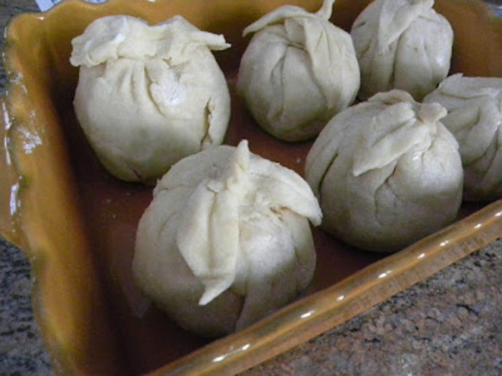 six apple dumplings setting in baking dish before being baked