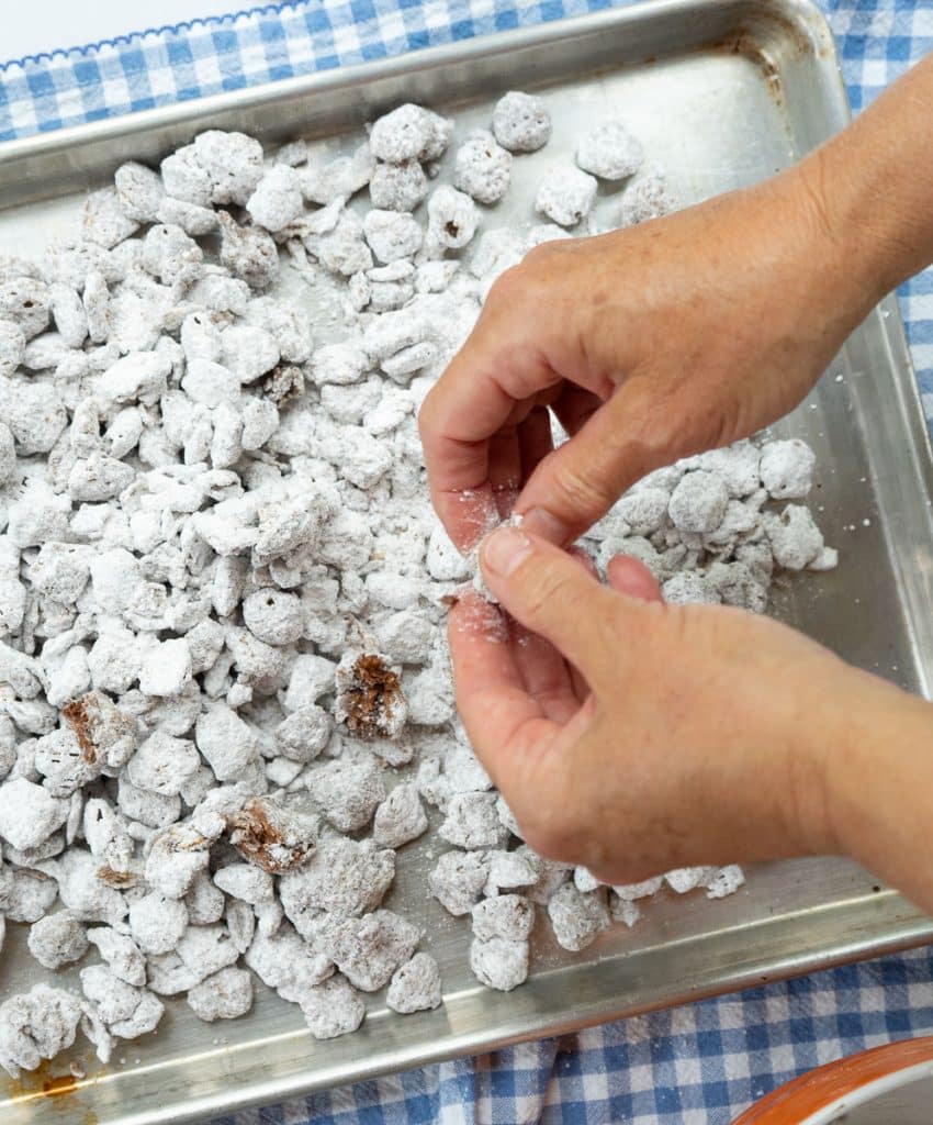 puppy chow on a cookie sheet, hands breaking up large chunks