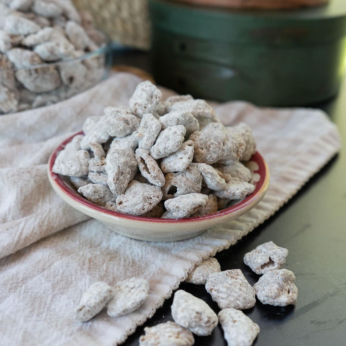 small bowl of puppy chow on a tan and white gingham cloth on a black table top. larger bowl of puppy chow in background