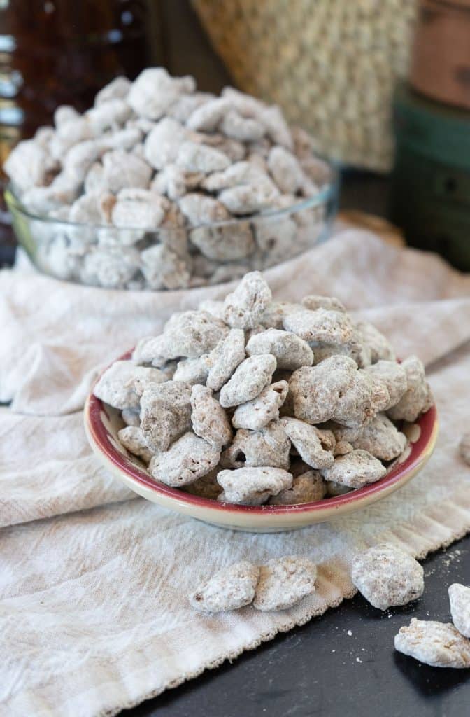 small bowl of puppy chow on a tan and white gingham cloth on a black table top. larger bowl of puppy chow in background