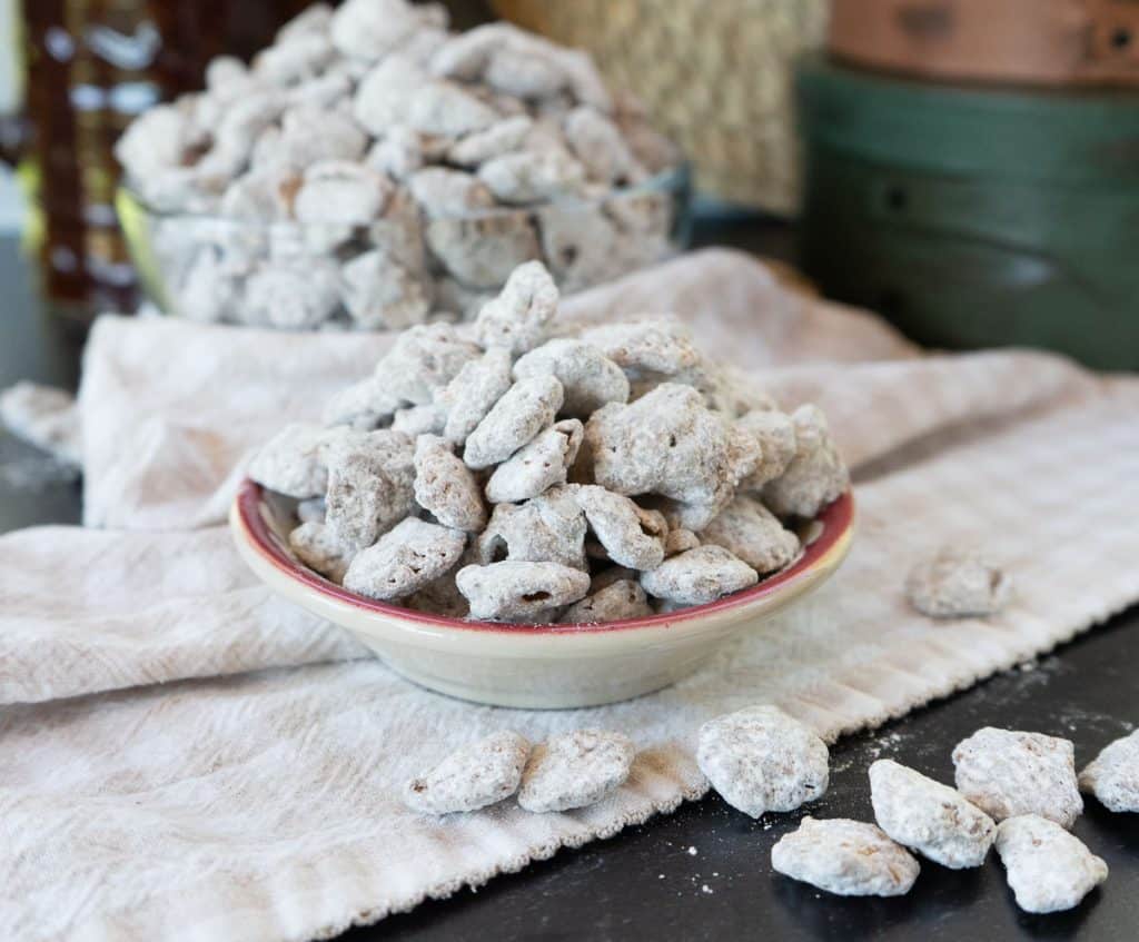 small bowl of puppy chow on a tan and white gingham cloth on a black table top. larger bowl of puppy chow in background
