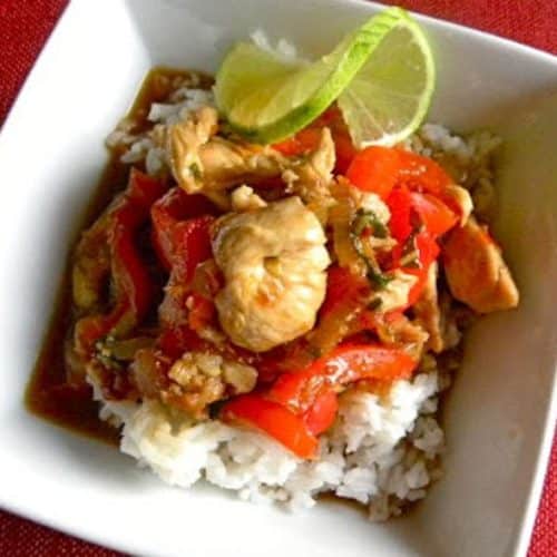 Thai Chicken in Sweet Chili Sauce over rice with a twist of lime in a white bowl on a red table