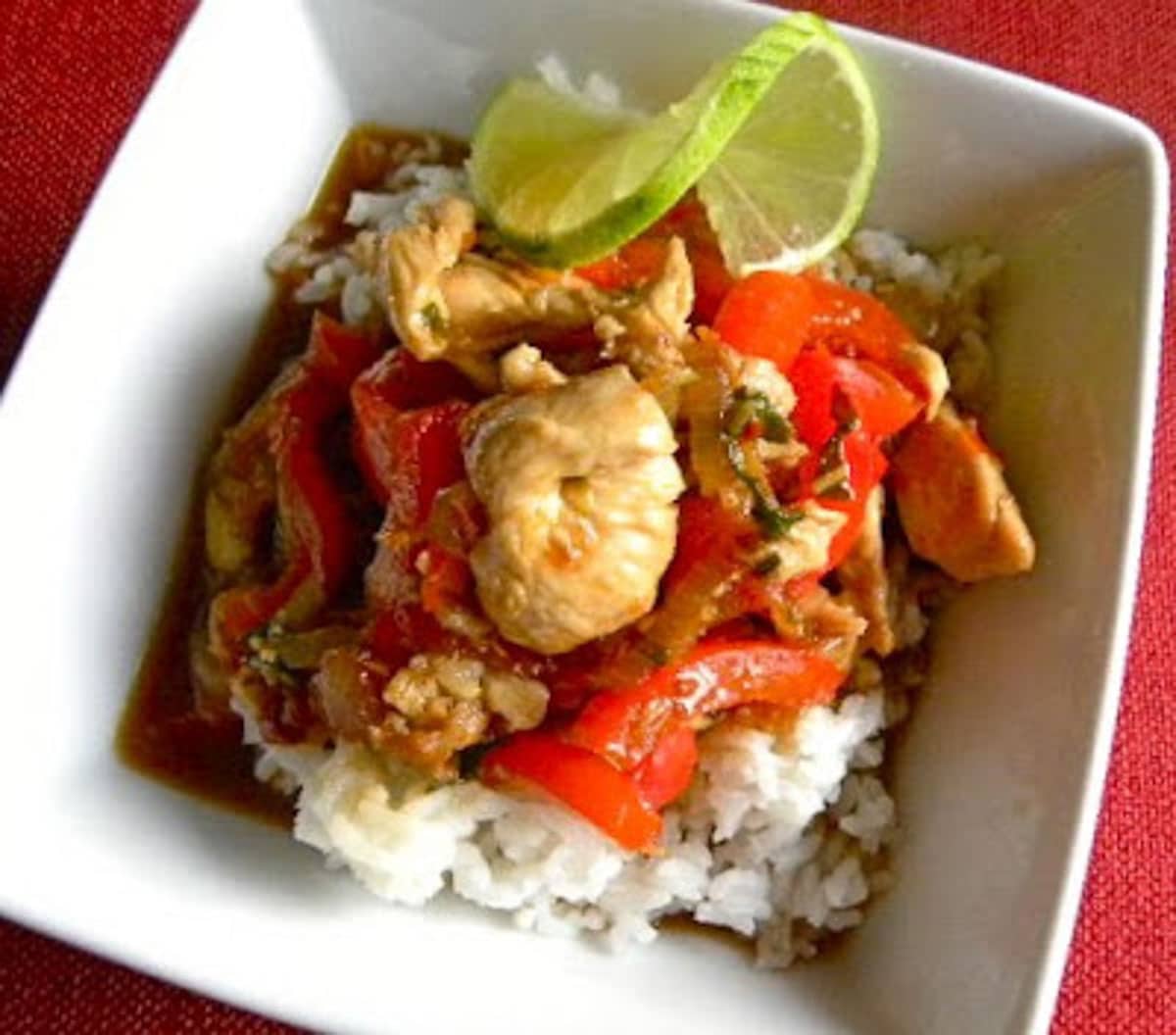 Thai Chicken in Sweet Chili Sauce over rice with a twist of lime in a white bowl on a red table