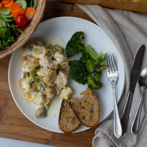 plated chicken tortellini bake on a white plate with broccoli and garlic toast, a dish of salad is in the upper left corner and the dish of tortellini is in the upper right corner of the photo
