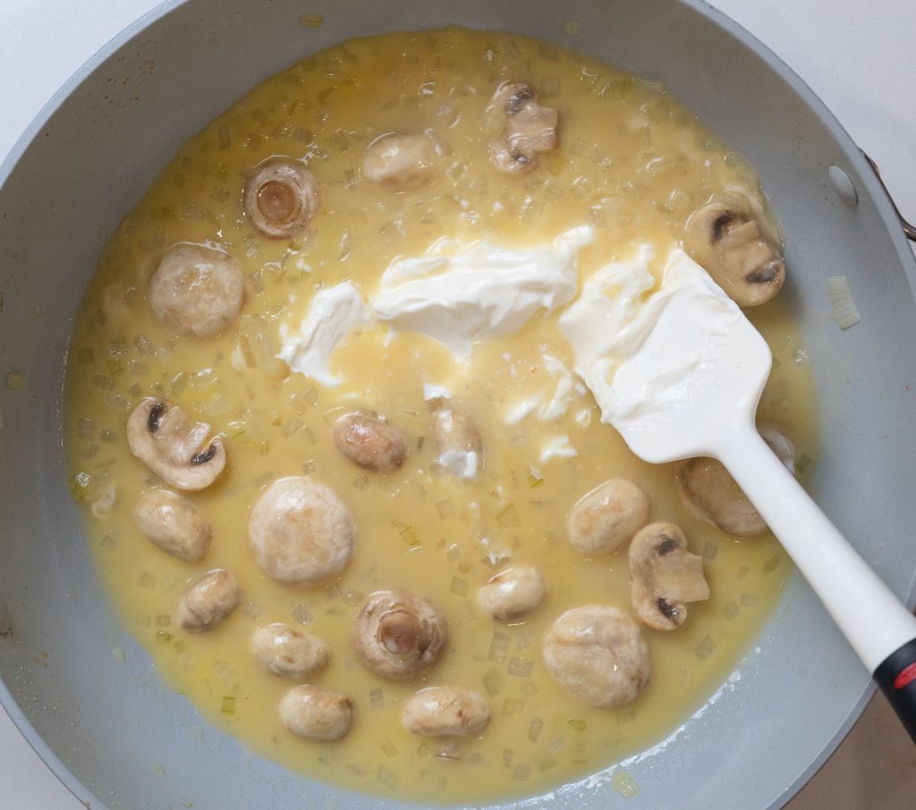 sour cream and cheese added to pan with mushroom, onion, and chicken broth. Spatula in pan on the right side of the photo.