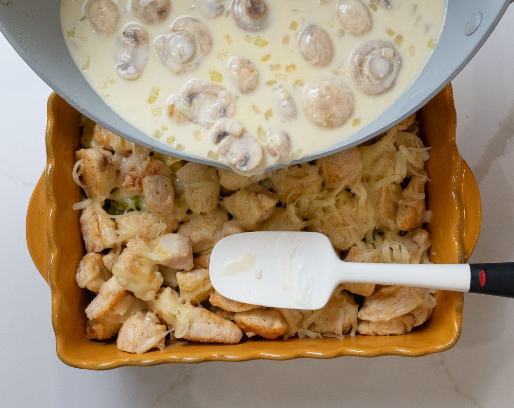 pouring sauce over chicken and cheese tortellini in a gold rectangle baking dish that is sitting on a white countertop