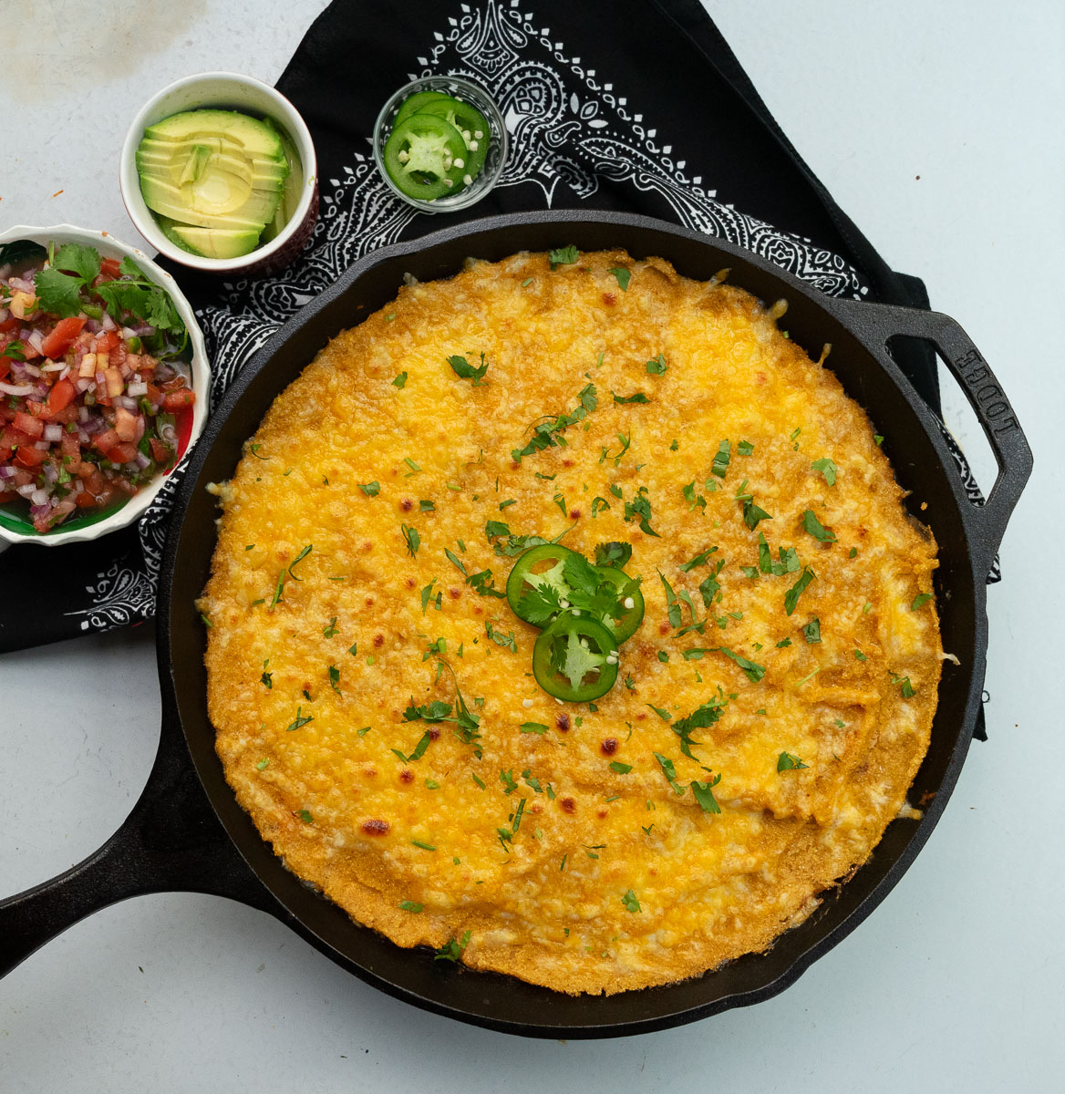 tamale pie in a cast iron skillet on a white counter top with salsa, jalepeno, and avocado slices in small bowl off to the side
