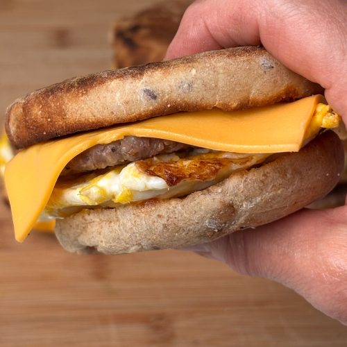 hand holding a sausage egg breakfast sandwich the background is a wood cutting board
