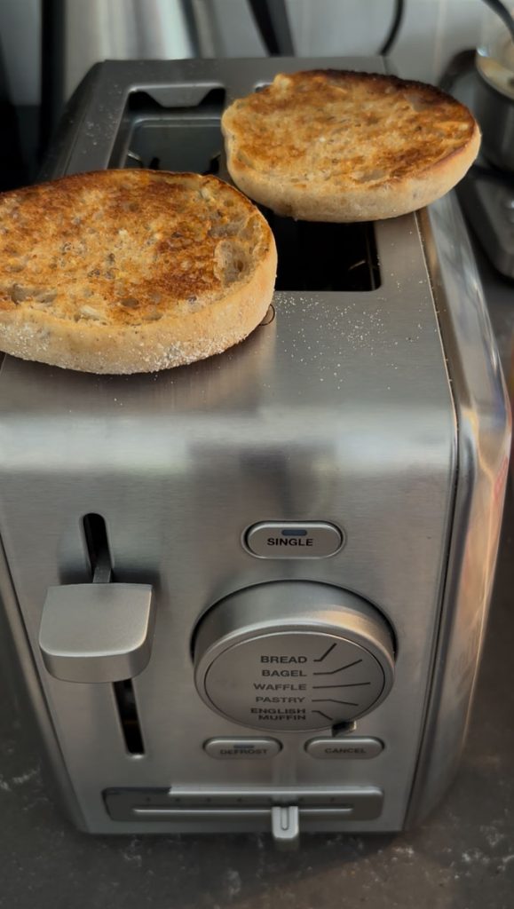 english muffin setting on top of a toaster, the english muffin is toasted. 