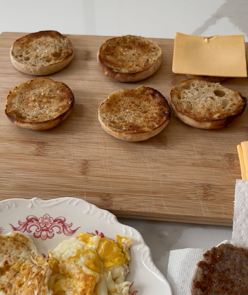 sausage and egg breakfast sandwich components set out on a wood cutting board to make serveral sandwiches