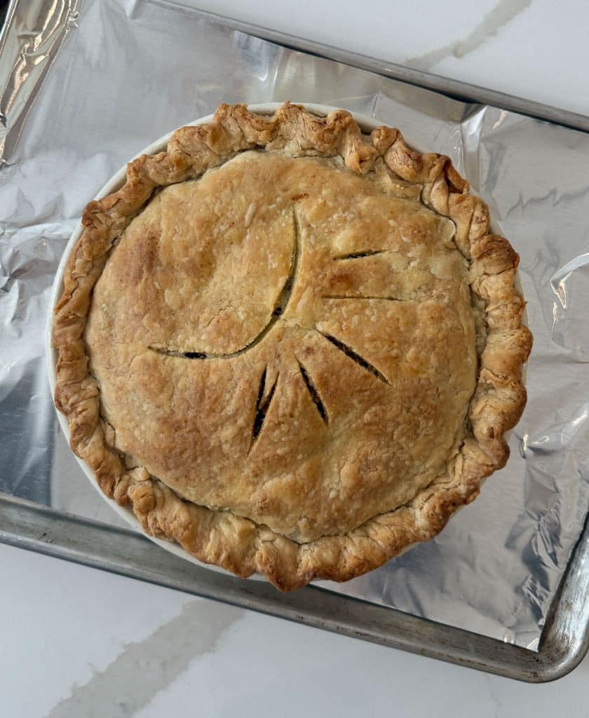 whole baked caramel apple crunch pie on a baking sheet on white countertop