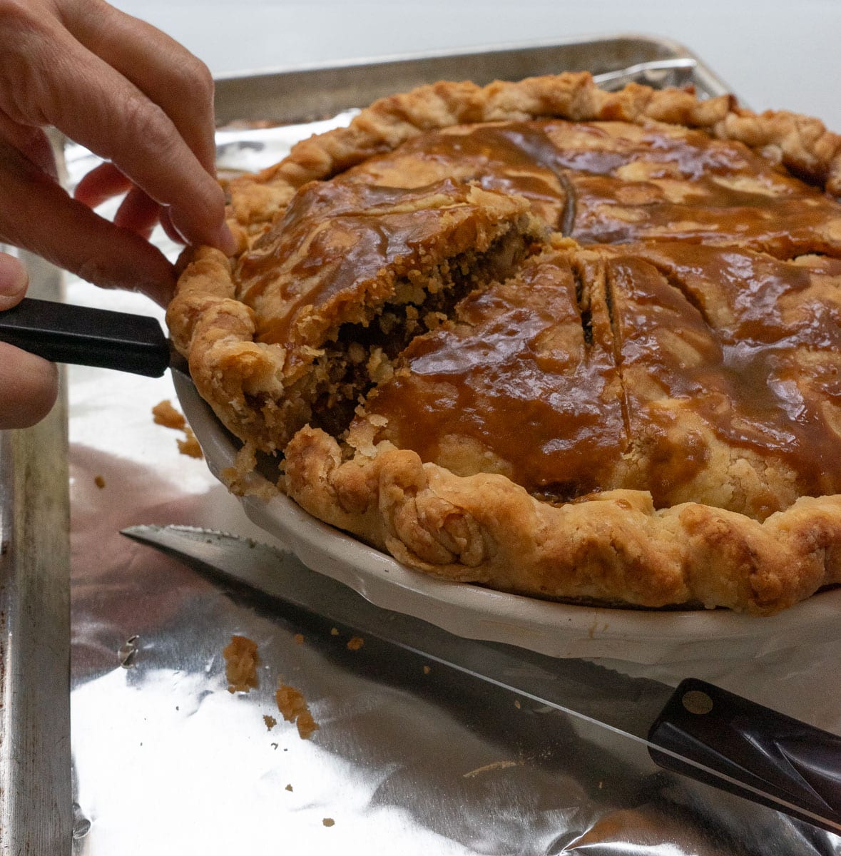 pulling out a slice of pie with a serving spatula, pie is sitting on a baking tray