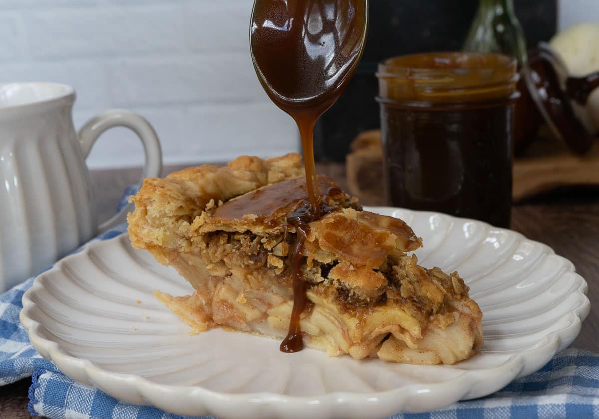 caramel apple crunch pie on a white plate with caramel sauce being poured over the pie