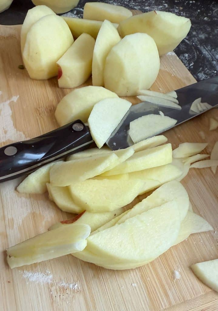 apples peeled and sliced on a wood cutting board knife laying in the middle