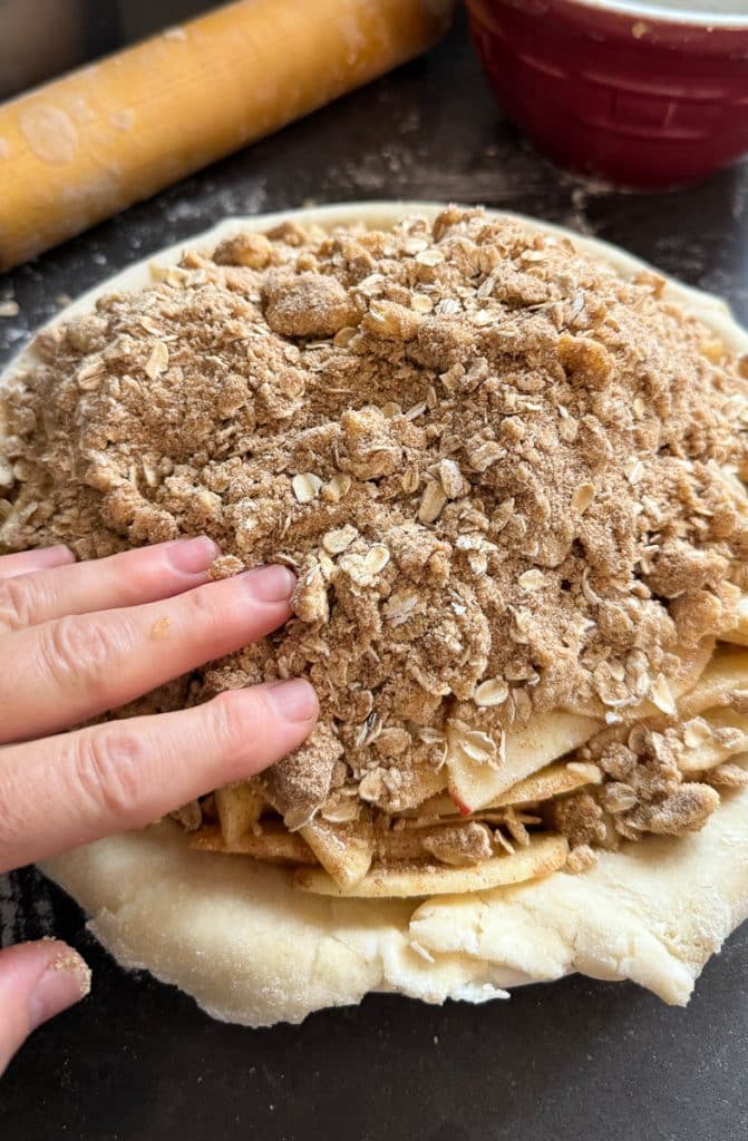 pouring brown sugar crumble over apples in pie crust