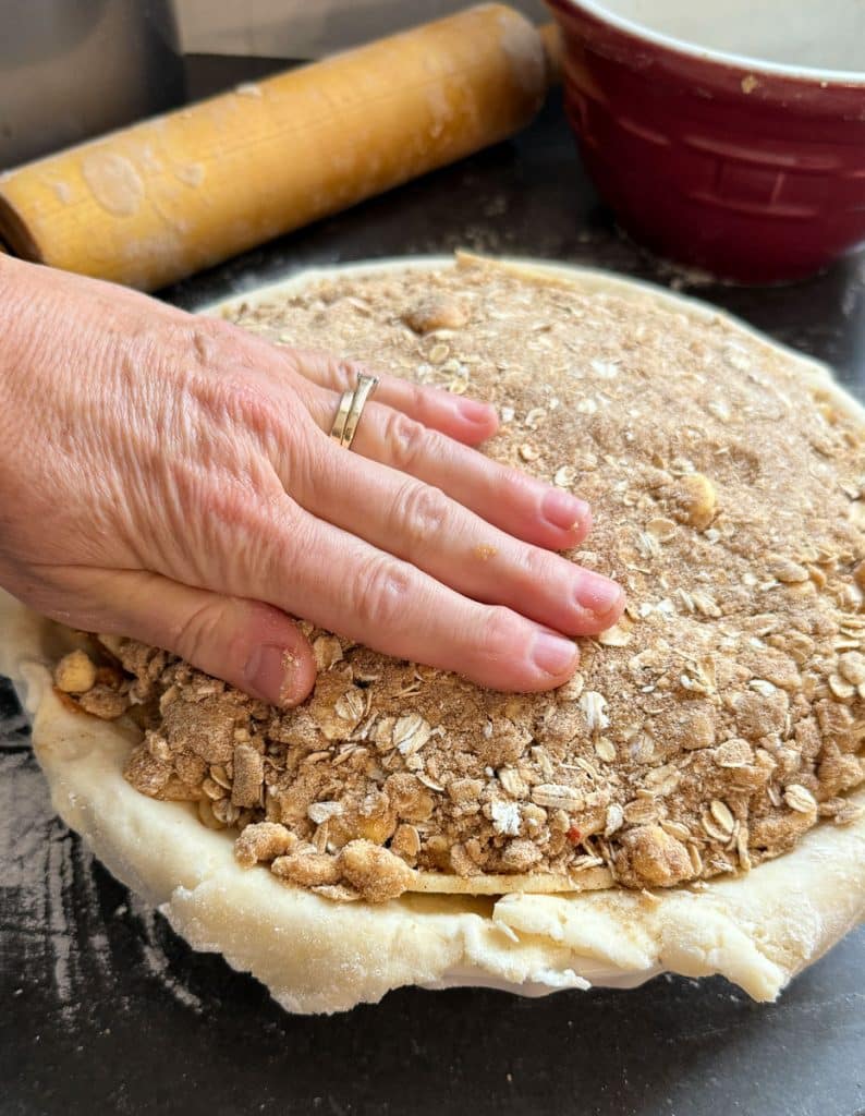 hand pressing the brown sugar and oat crumble layer into the apples in the pie plate