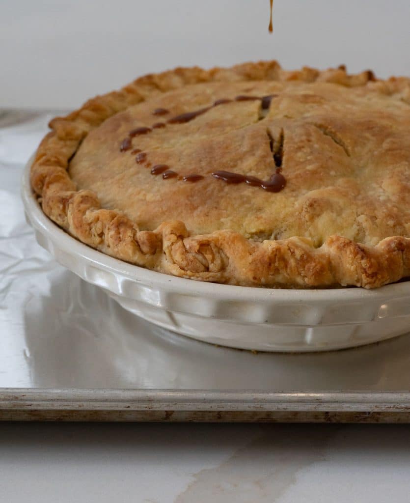 baked pie sitting on a cookie sheet with caramel being drizzled over the pie