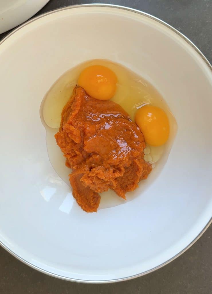 pumpkin puree and two eggs in a white mixing bowl 