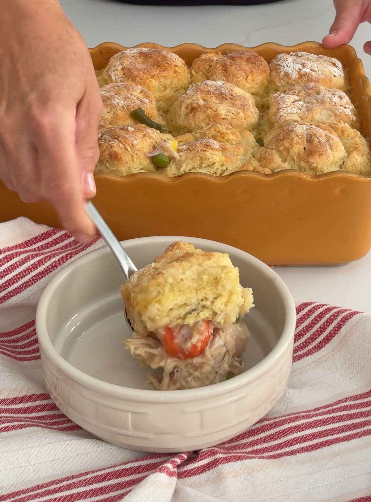 Chicken and biscuits being served from baking dish to a bowl