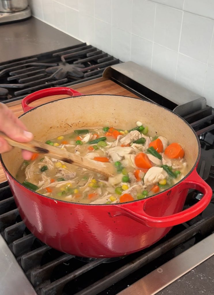 red dutch oven with a wooden spoon stirring chicken stew for chicken and biscuits
