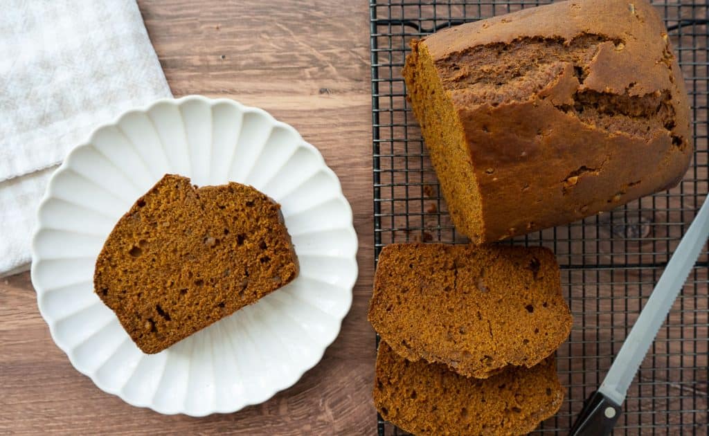 slice of pumpkin gingerbread on a white plate, next to the loaf of bread on a cooking rack