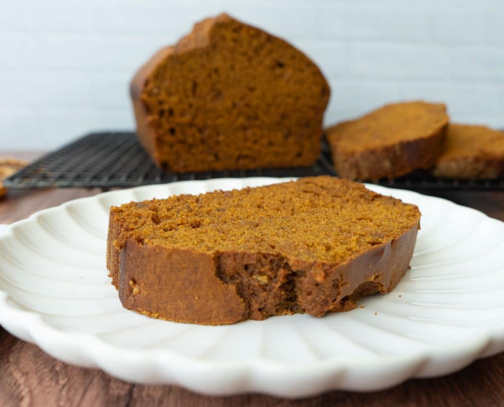 slice of pumpkin gingerbread on a white plate, next to the loaf of bread on a cooking rack