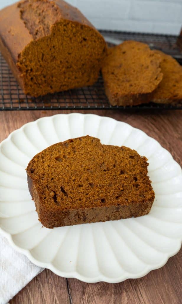 slice of pumpkin gingerbread on a white plate, next to the loaf of bread on a cooking rack
