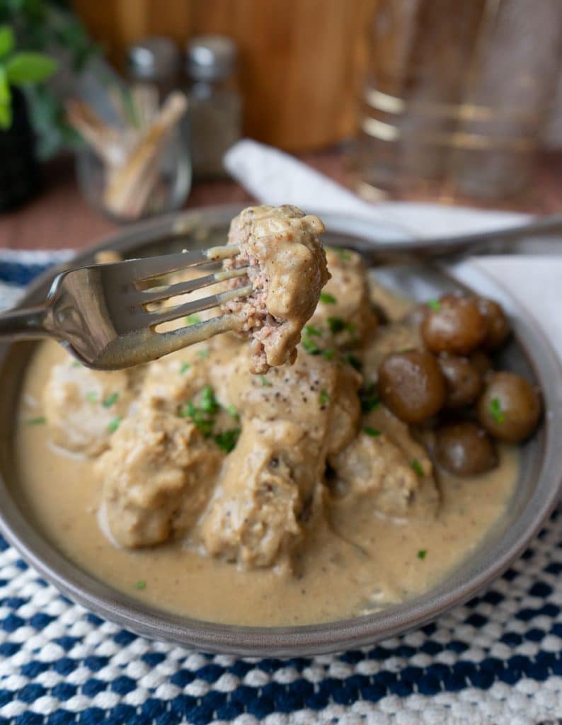 plate of swedish meatballs on a dinner plate at a table with a fork holding a meatball over the plate