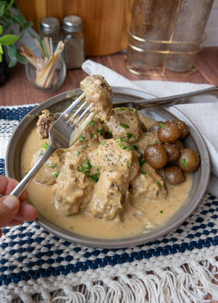 plate of swedish meatballs on dinner table with a fork and meatball being held over the plate