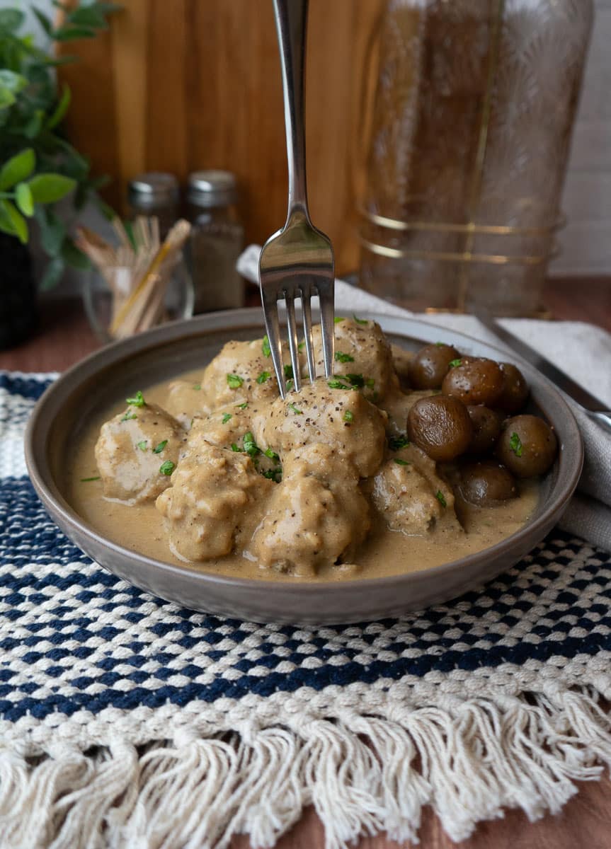 plate of swedish meatballs on a blue and tan pattern placemat with a fork sticking out of the center of the plate