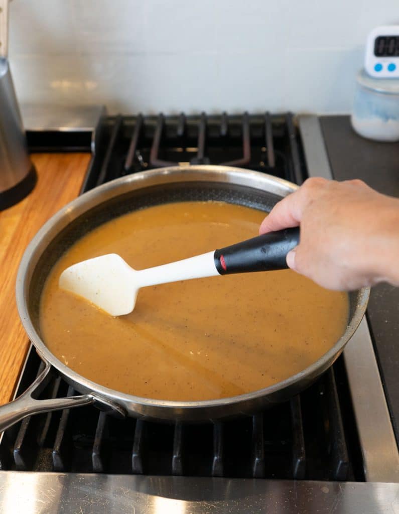 stirring gravy for swedish meatballs with a white spatula on stovetop