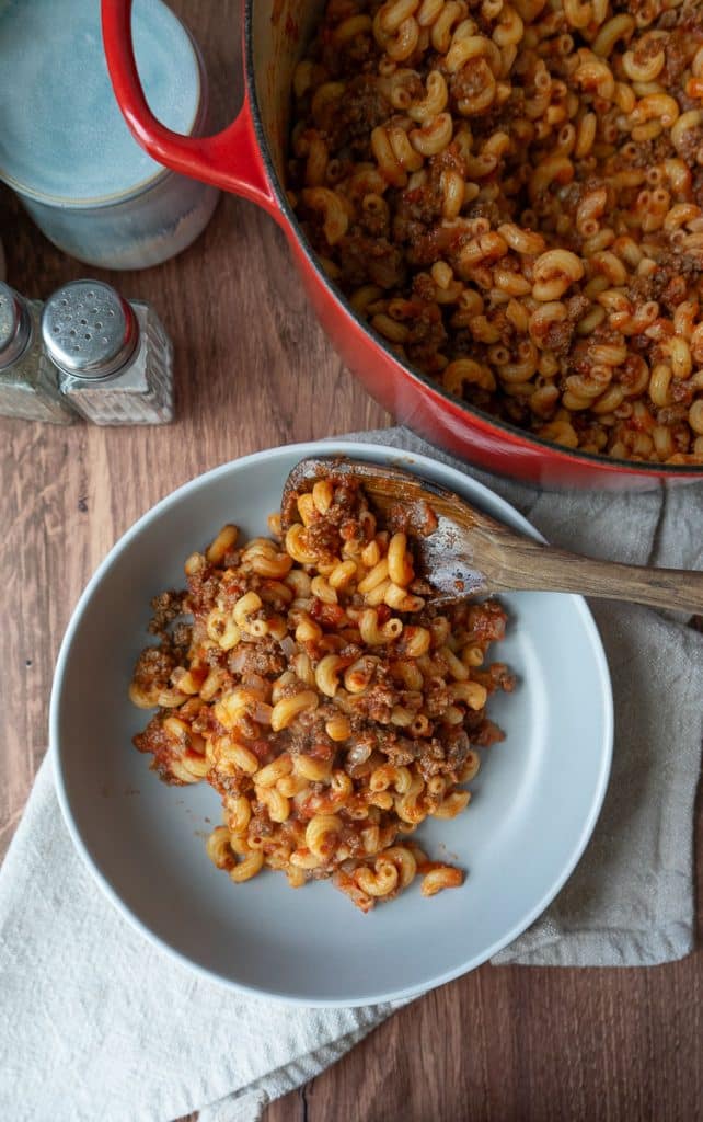 a plate off goulash with a fork on the plate in front of the dutch oven full of goulash salt and pepper shakers are off to the left upper side