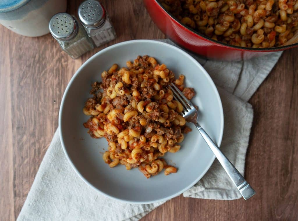 a plate off goulash with a fork on the plate in front of the dutch oven full of goulash salt and pepper shakers are off to the left upper side