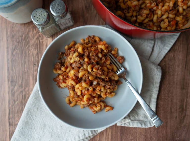 a plate off goulash with a fork on the plate in front of the dutch oven full of goulash salt and pepper shakers are off to the left upper side