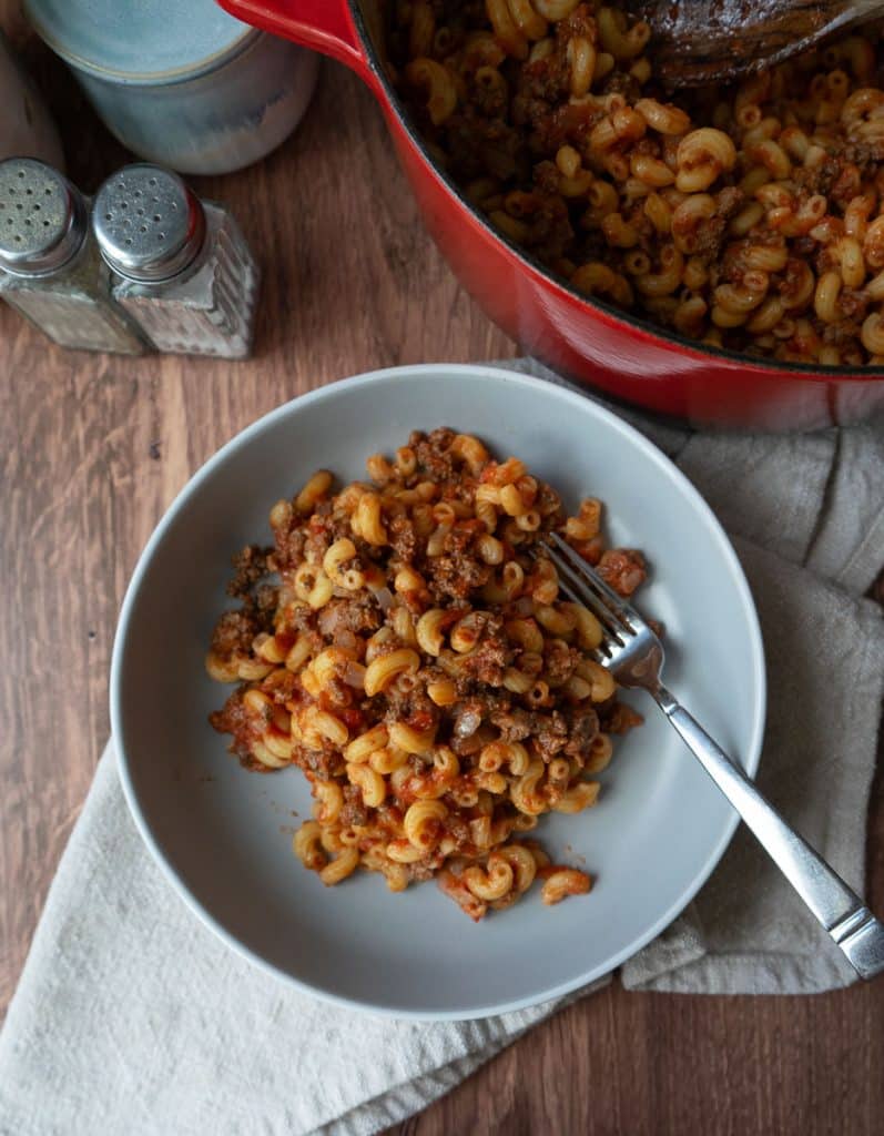 a plate off goulash with a fork on the plate in front of the dutch oven full of goulash salt and pepper shakers are off to the left upper side